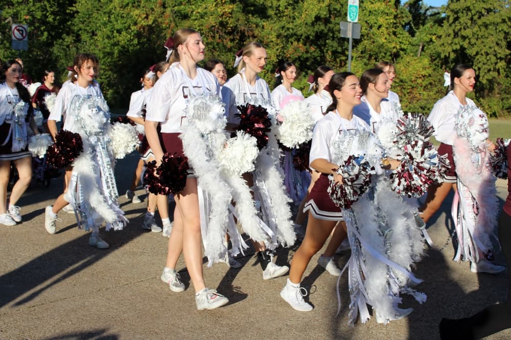 Girls wearing long white homecoming mums walking in a parade. 