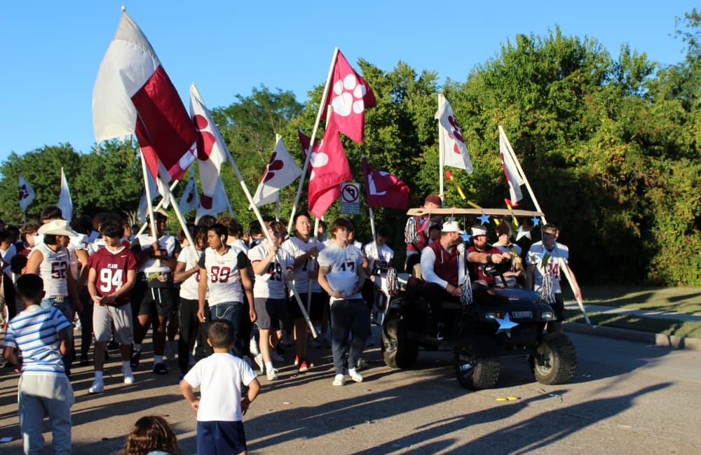 Teens walking in a parade carrying large marroon and white flags. 