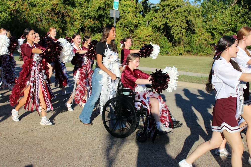 Girl being pushed in a parade carrying pompoms. 