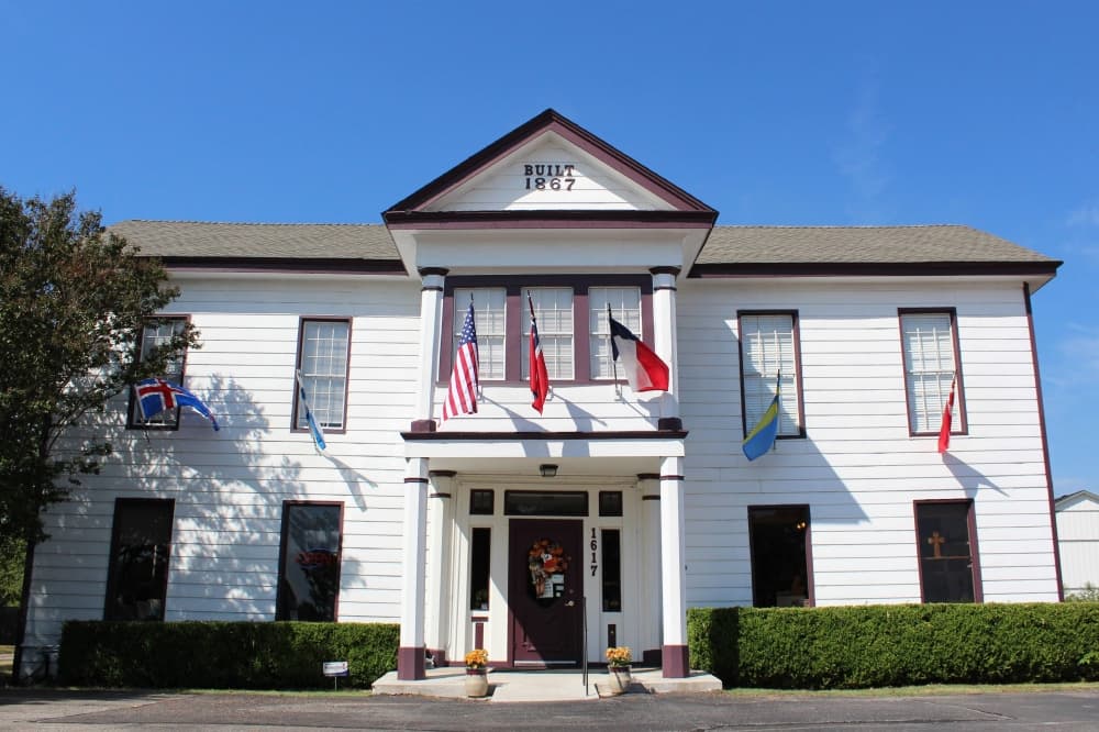 Exterior of two-story house with a variety of national flags hanging over the door. 