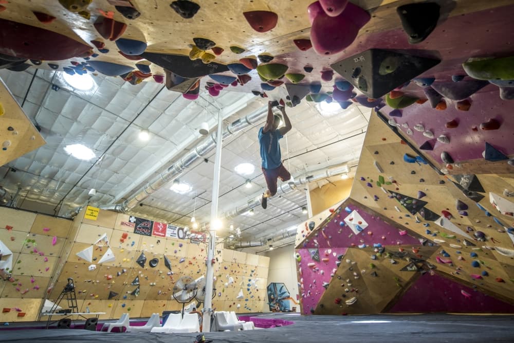 A man is climbing an indoor climbing center, dangling in the air. 