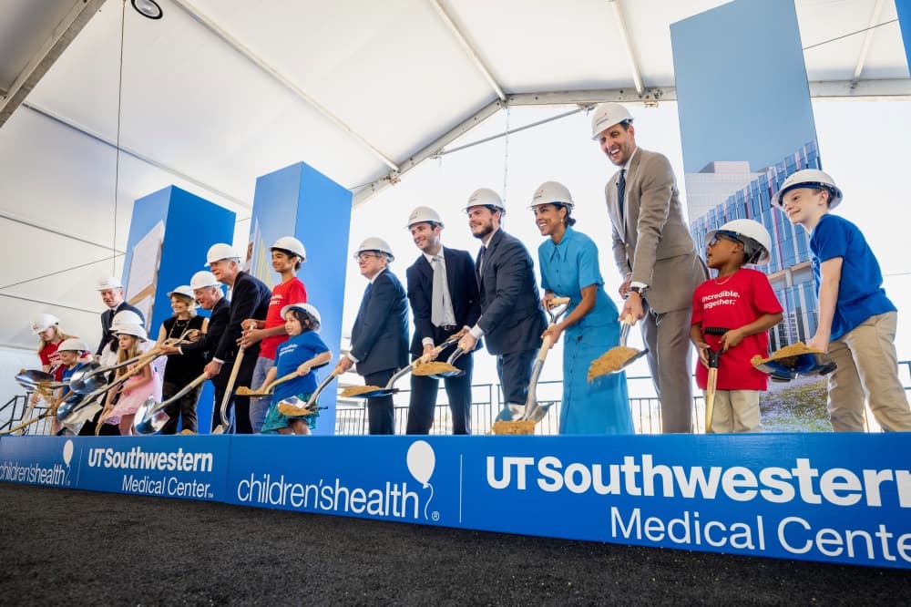 A line of medical officials and community members are lined along a patch of dirt with shovels. 