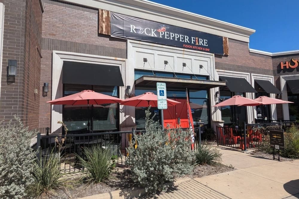 Exterior of building with Rock Pepper Fire signage and tables on a patio with umbrella coverings. 