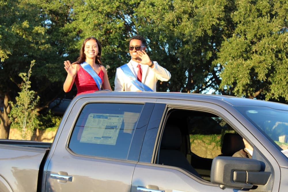 Male and female waving from the back of a truck in a parade. 
