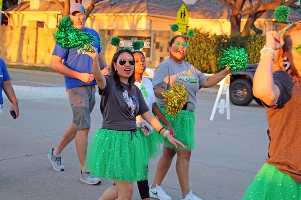 People wearing green skirts and headbands in a parade.