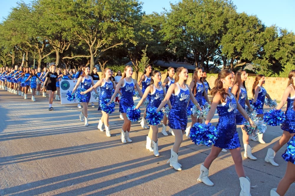 Drill team marching in a parade wearing blue uniforms. 