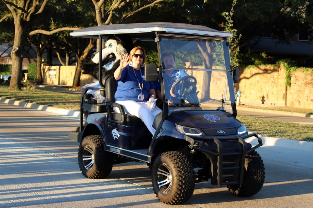 Female waving from a golf cart in a parade. 
