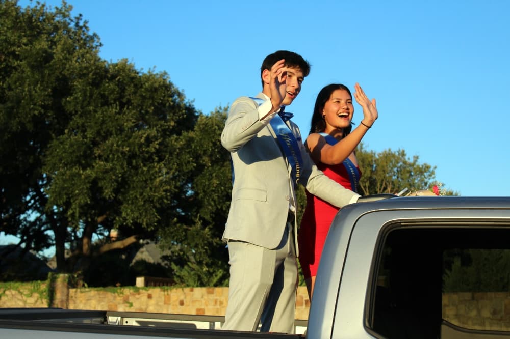 Male and female waving from the back of a truck in a parade. 