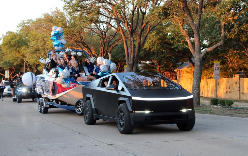 Tesla truck towing a boat filled with students in a parade.