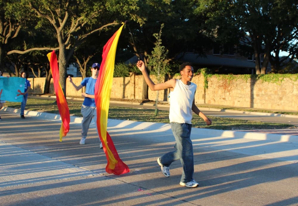 Teens twirling flags in a parade. 