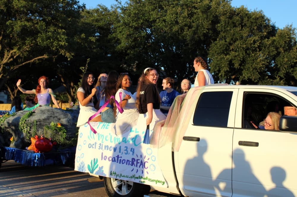 Students riding in the back of a white truck in a parade. 