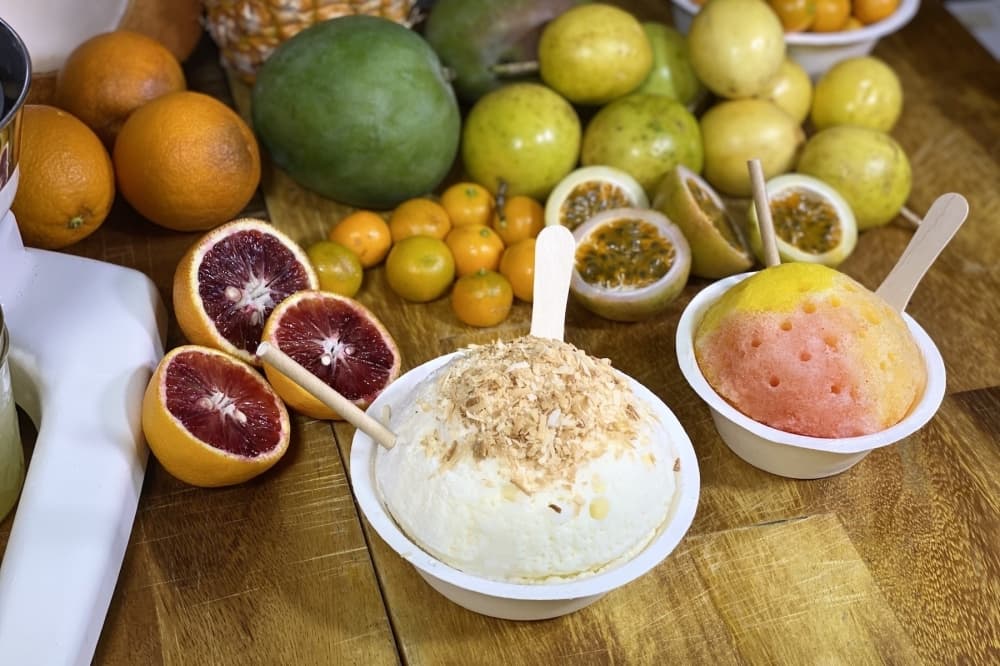 The Haleakala, left, comes with leche, coconut and a snow cap. The Sunset Beach, right, is made with passion orange, mango and guava syrups. (Courtesy Ululani’s Hawaiian Shave Ice) 