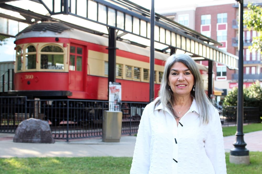 Female standing in front of an old train car that is on display in a park. 