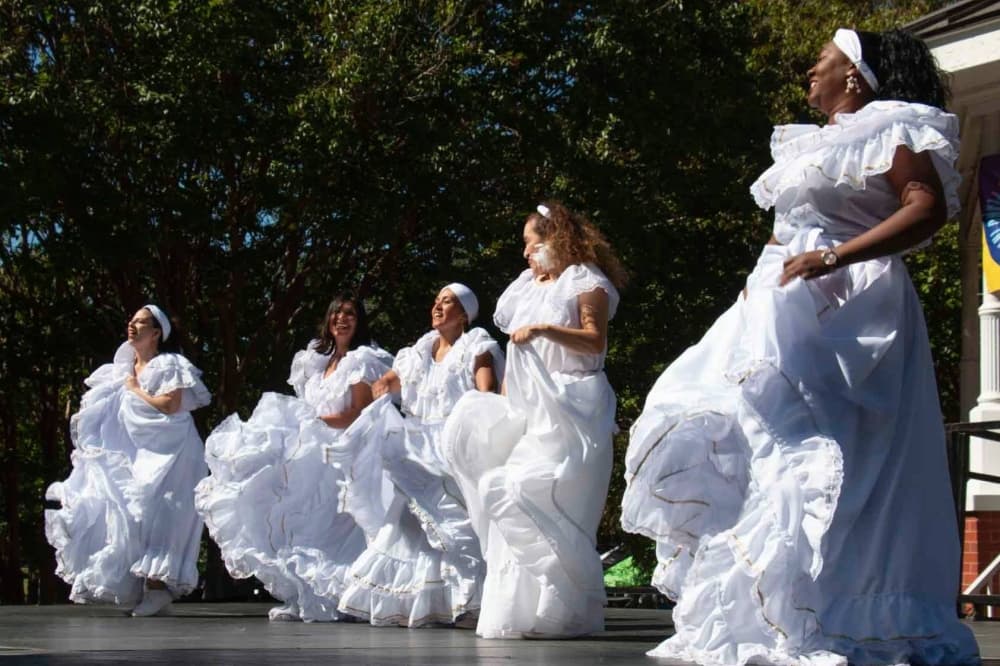 Women dancing in floor-length white cultural dresses. 