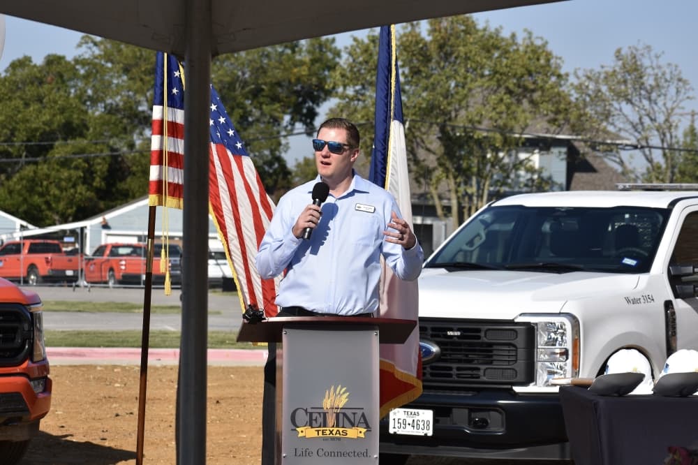 a man speaks behind a podium at an outdoor groundbreaking ceremony