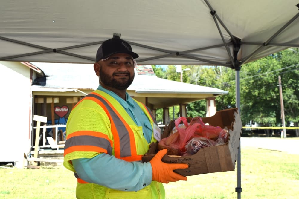 A volunteer smiles and holds a box filled with food at a distribution event.