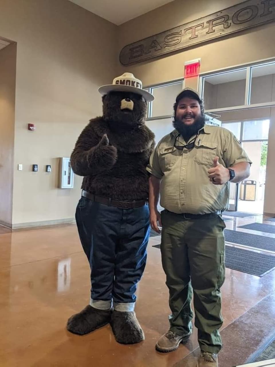 A man stands next to Smokey Bear, both giving a thumbs up, at a special event.