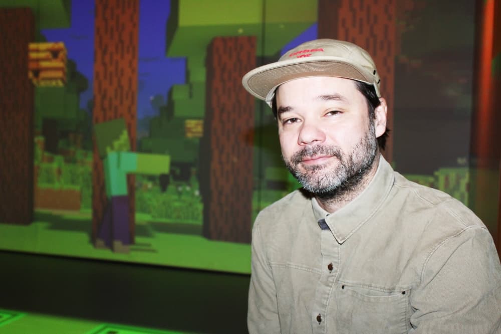 Man wearing tan button down shirt and ball cap in front of Minecraft game projection.