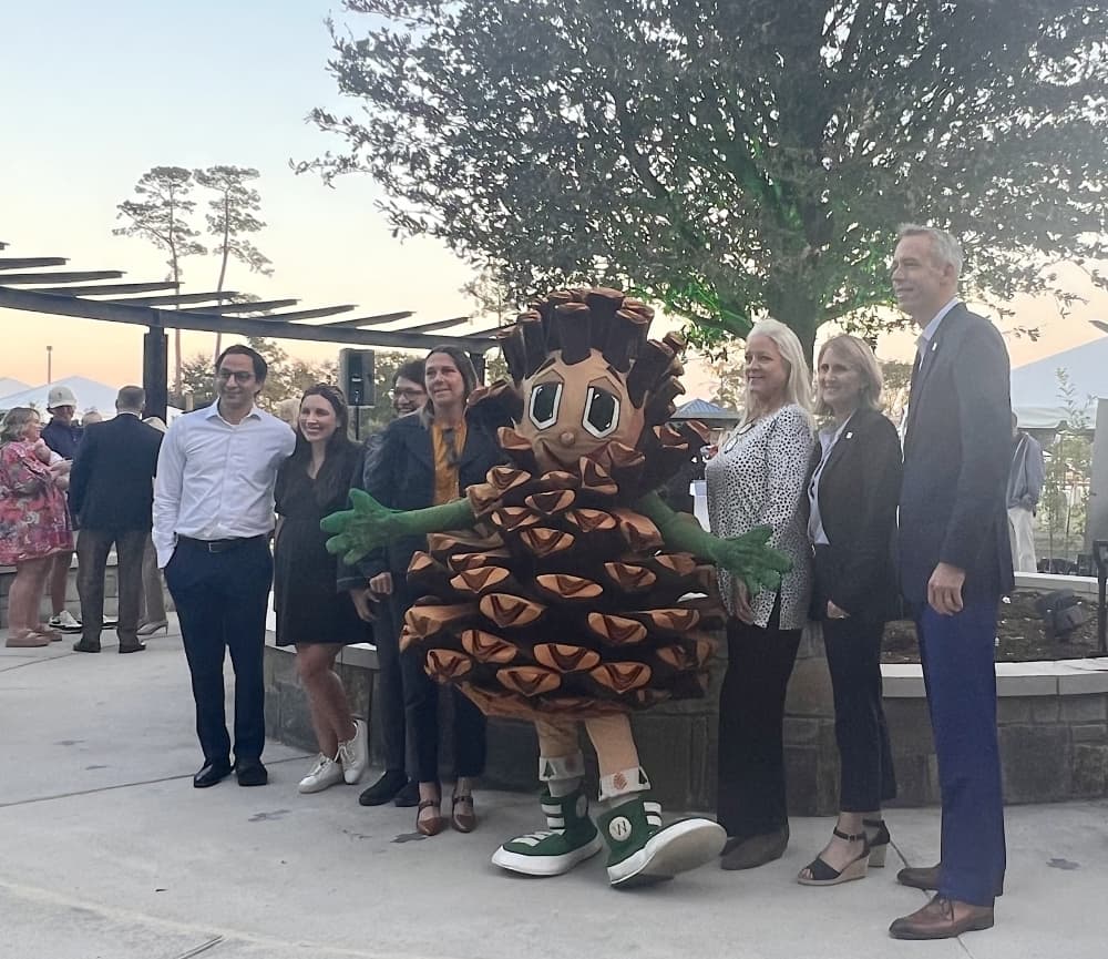 people and a pine cone mascot gathered by a tree