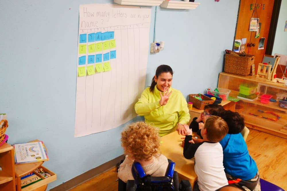 An image of a caretaker and a few children in a classroom setting. 