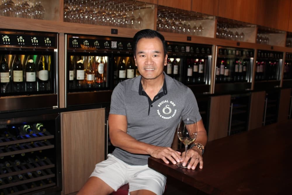 Man wearing Social Oak logo shirt sitting in front of wine dispensers. 
