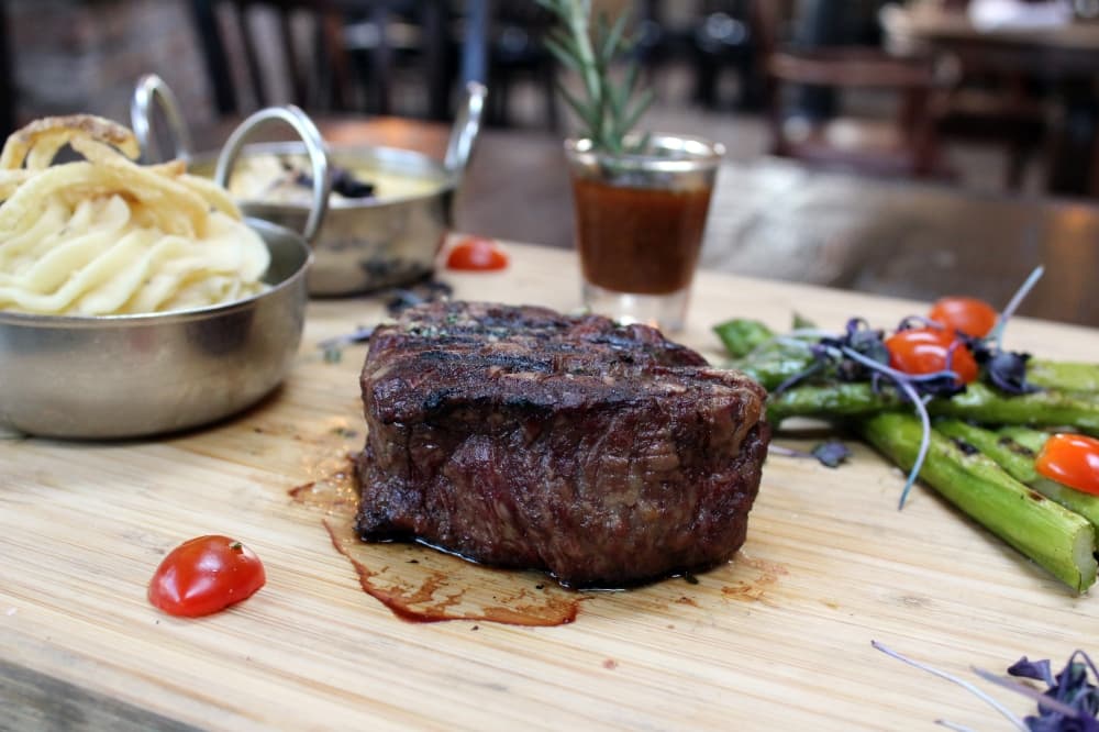 Steak on a wooden board with potatoes and asparagus side dishes. 