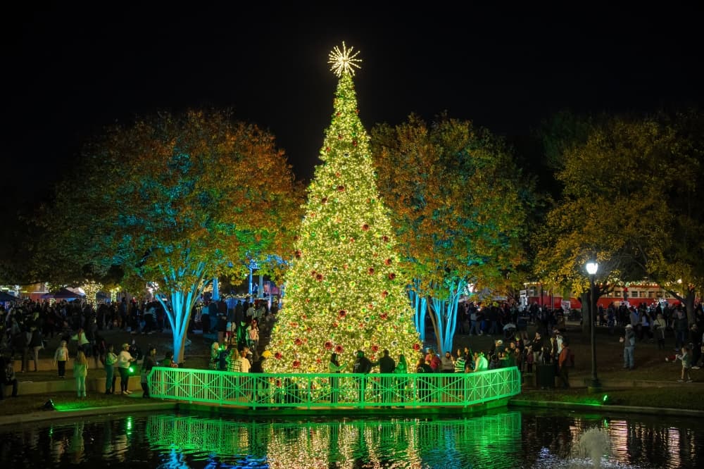 Christmas tree at night with lights reflecting in nearby pond. 