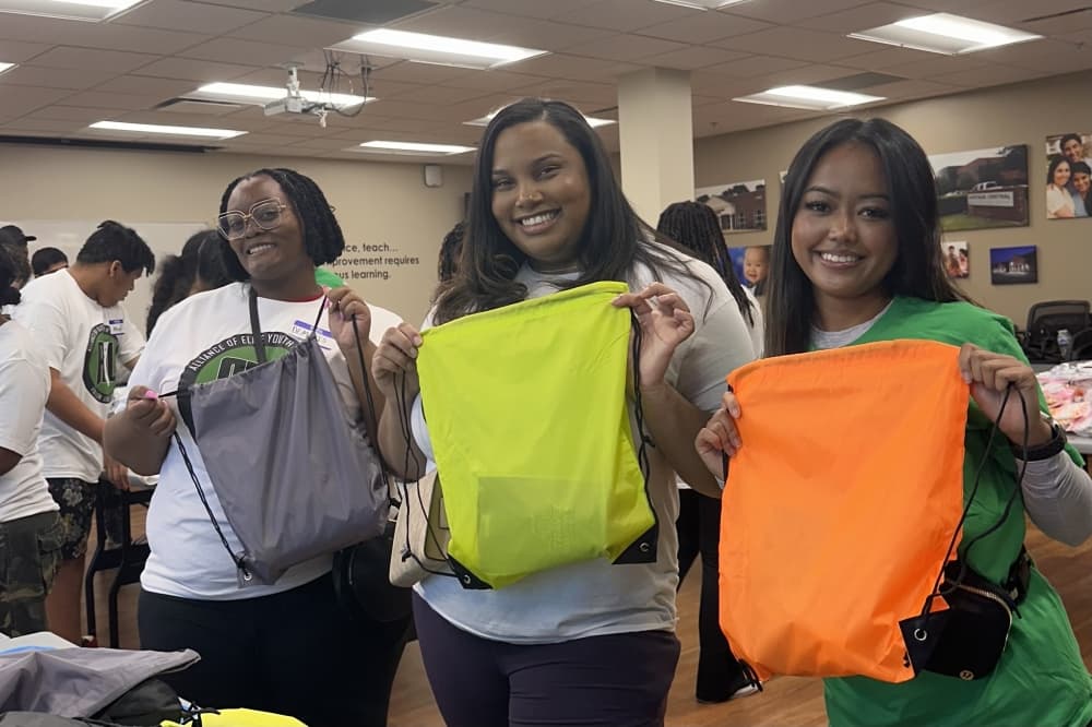 Three AEYL members holding string backpacks