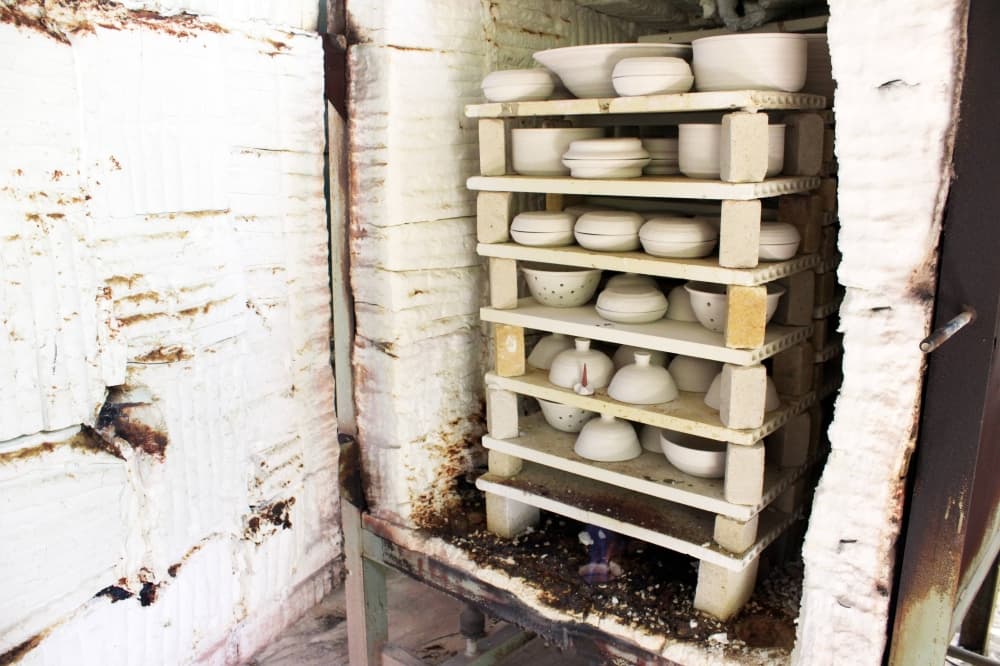 Open upright kiln holding racks of pottery. 