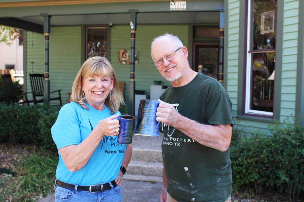 Male and female standing in front of historic building holding hand made pottery mugs.
