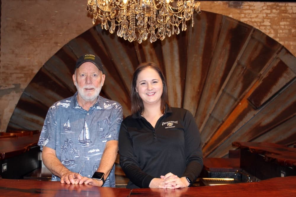 Male and female standing in front of historic architectural elements and under a crystal chandelier inside restaurant 
