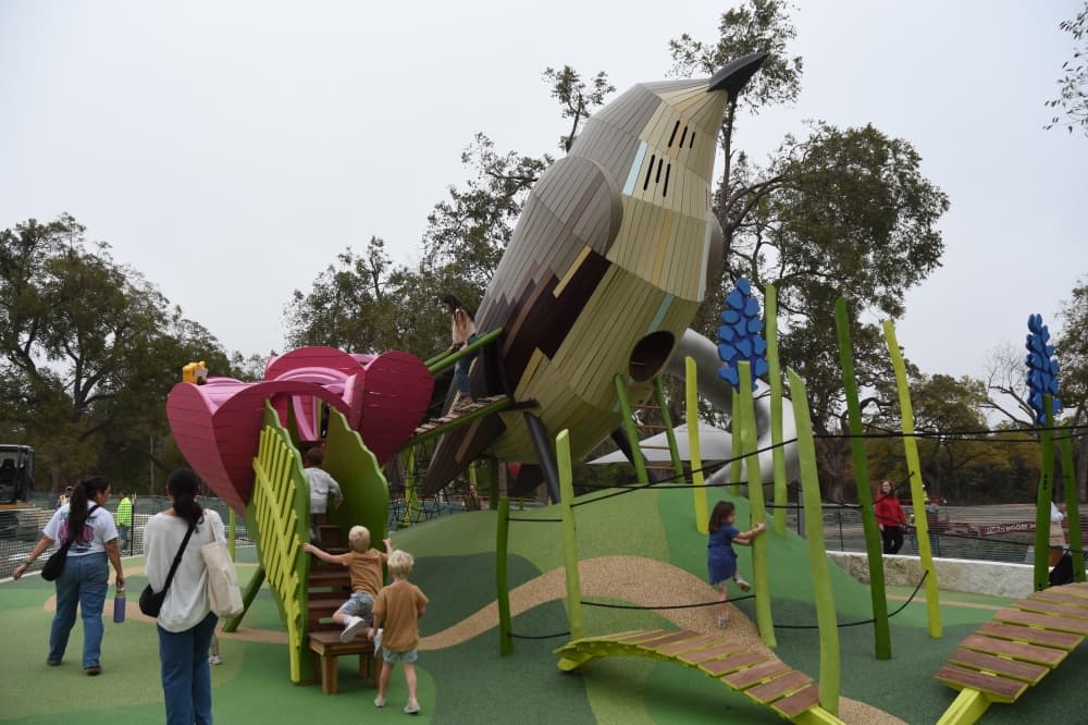 Children play on a playground, heading up stairs into a bird shaped structure. 