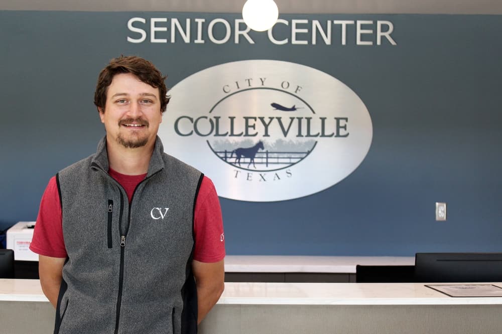 Male standing in front of a wall with Colleyville Senior Center signage. 