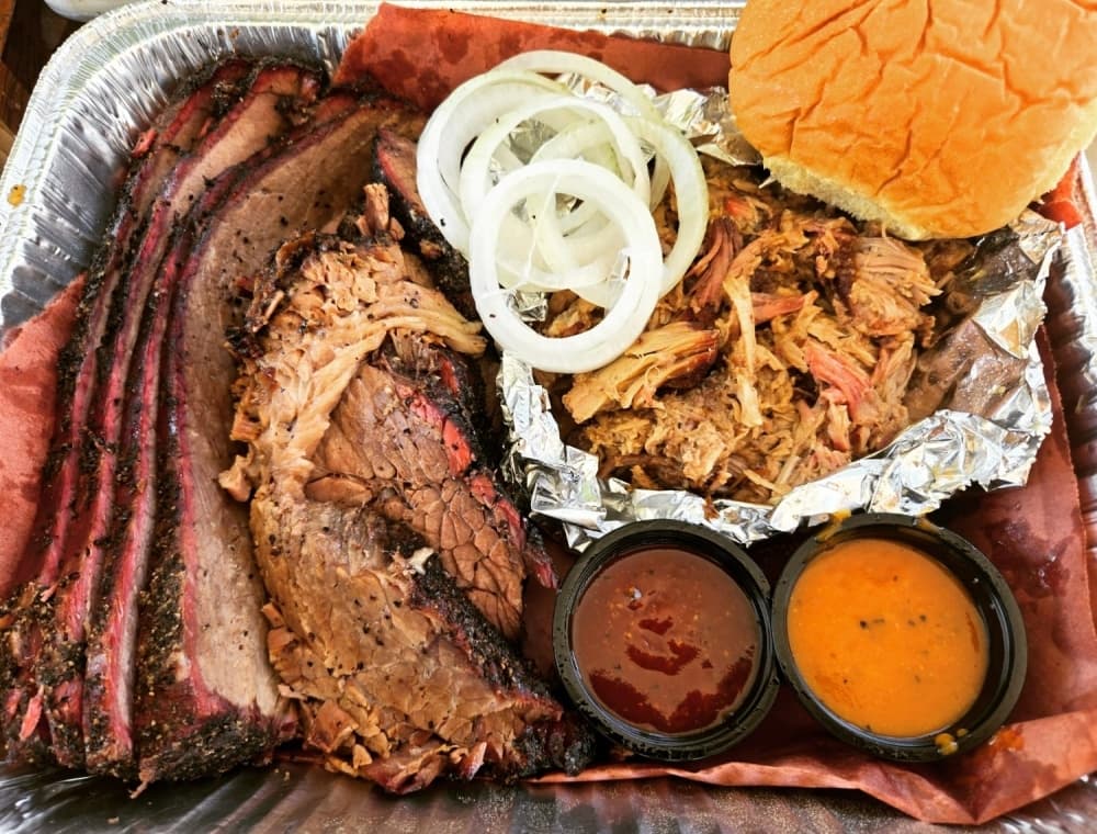 A tray of meat is shown with sauces, onions and bread.