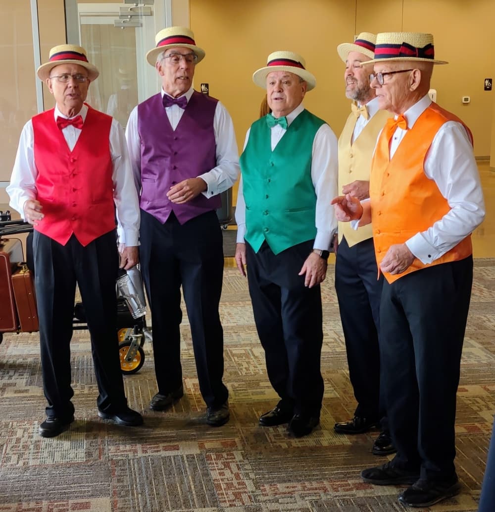 A barbershop quartet is shown while singing and wearing hats and colorful vests.