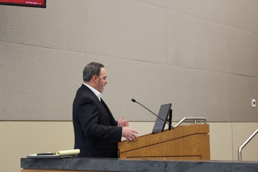 A man speaks at a podium in front of city council. 