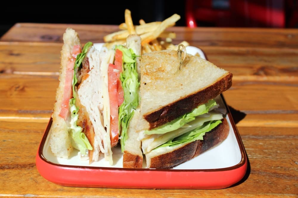 Sandwich with turkey, tomatoes and lettuce and side of french fries. 