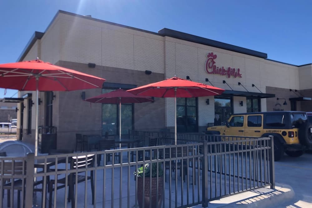 Exterior of a Chick Fil A with a patio with red umbrellas over tables. 