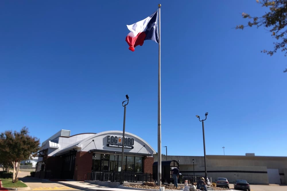 Exterior of a building with Egg n Bird signage and a tall flag pole with a Texas state flag. 