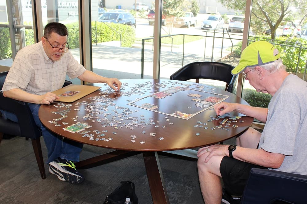Two males working on a puzzle on a table. 