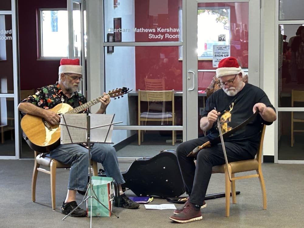 Two people wearing Santa caps play music at a previous open house.
