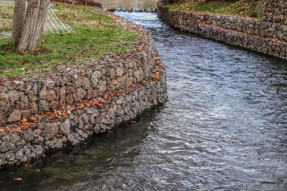 A Gabion wall is constructed using wire cages filled with rocks where vegetation is intentionally planted within the gaps between stones to allow plants to grow. (Courtesy Adobe Stock)