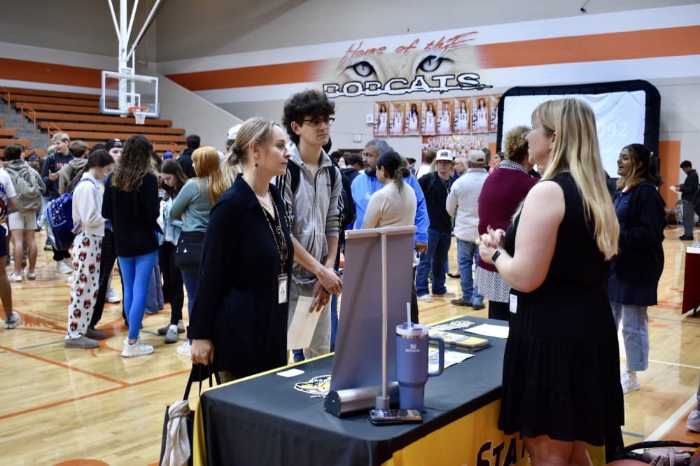 a mother and son speak to a college advisor at a table