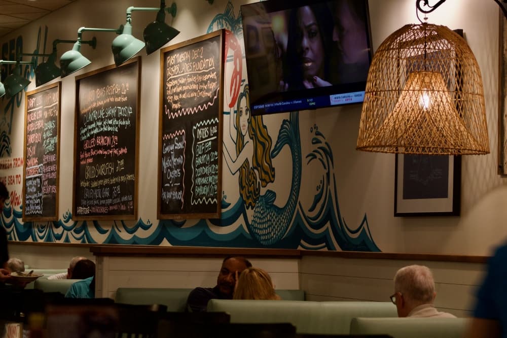 Drawing of Mermaid on wall with chalkboards and people seated for dinner.