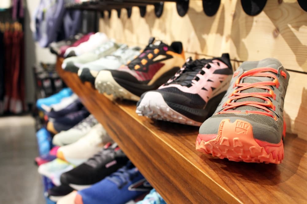 Variety of running shoes displayed on wooden shelves in a store. 