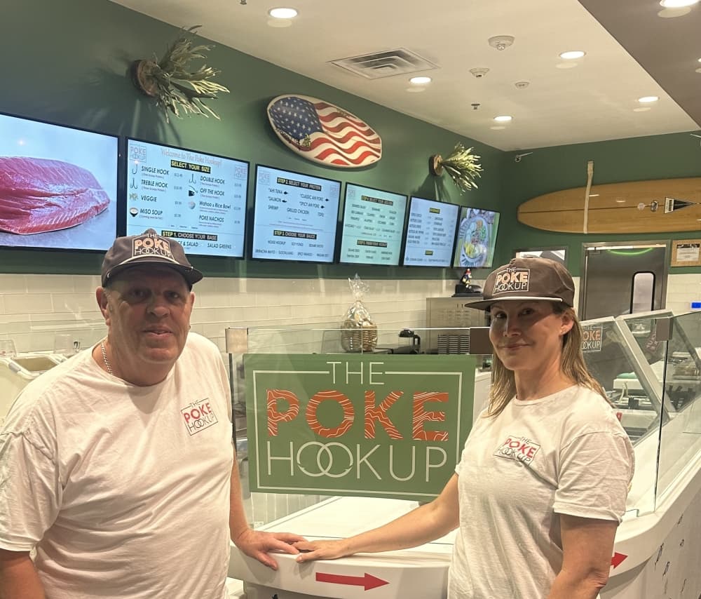 man and woman standing in front of "the poke hookup" sign 