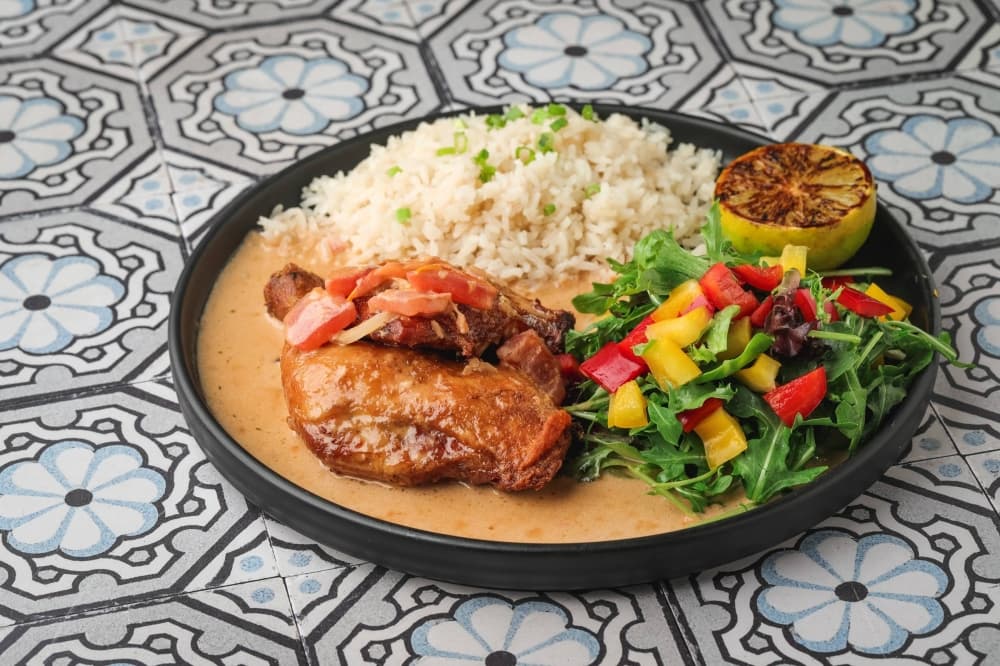 Chicken covered in a sauce with sides of rice and salad. 