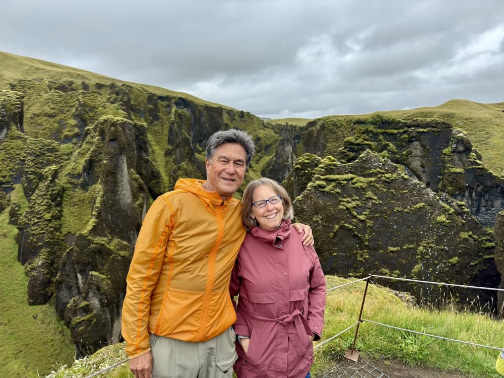 A man and a woman stand in front of a mountainous vista.