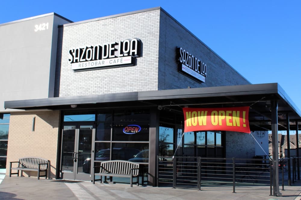 Exterior of building with Sazon De Loa sign and Now Open banner.