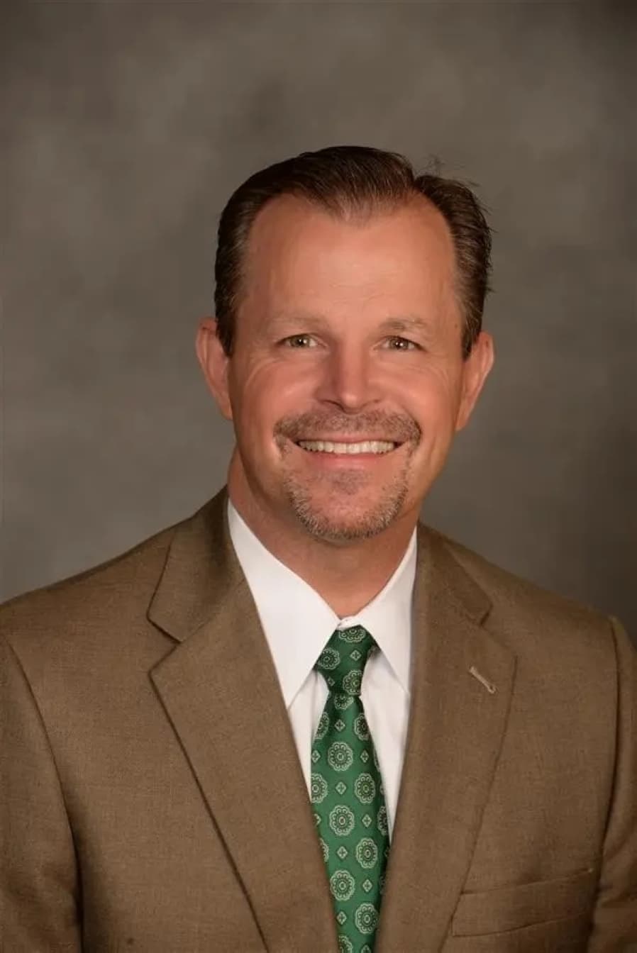 a headshot of a man in a tan suit and green tie